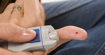 Someone holding a device to measure blood sugar for diabetes, with a blood of drop on the finger