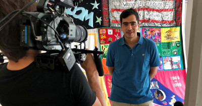 Jose of Fast Track Cities resenting to a video camera in front of a quilt