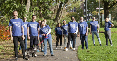 Large group of Ribbon Walk people in THT shirts in park with dog