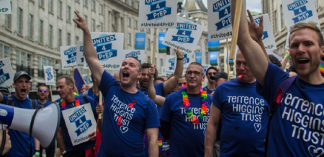 People marching during Pride event, holding banners calling for access to PrEP
