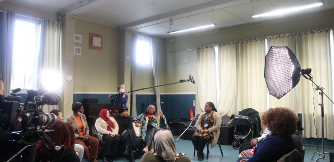 Image of a group of women of Black African and Caribbean heritage in discussion with a sexual health nurse. Recording equipment can be seen in the shot. 