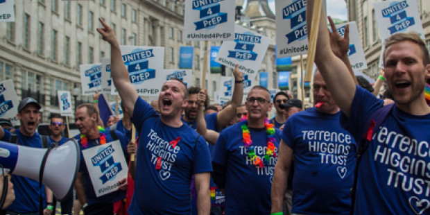 People marching during Pride event, holding banners calling for access to PrEP